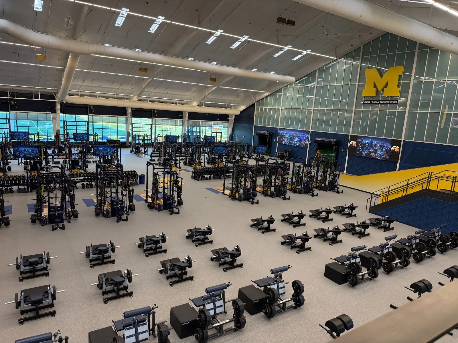 Wide view of a university football weight room with LED displays above every rack